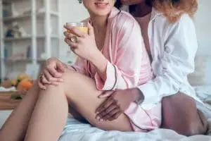 amour-relations-main-femme-peau-foncee-chemise-blanche-cuisse-petite-amie-caucasienne-lingerie-rose-assis-lit-matin